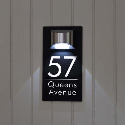 Black LED house number plaque 57 Queens Avenue, lit custom sign on light grey wooden wall
