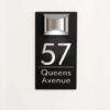 Black personalised house number sign 57 Queens Avenue, matte plaque with silver letters on white background